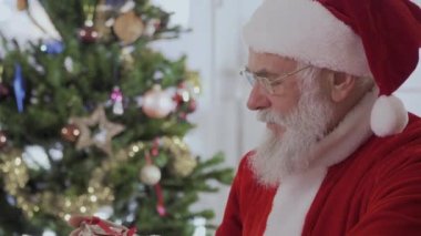 Noel Baba oturup masada, mevcut kutusuna bakın, Hediyelik göstermek ve kamera mevcut vermek.