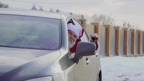 穿着红色服装和帽子的圣诞老人坐在他的新灰色汽车和摇头车钥匙 老家伙刚买了辆新车 周围是雪 — 图库视频影像