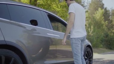 Genç adam modern araba kapısını açamıyor. Adam omuz silkiyor ve arabanın içinde sandalyenle opn pencerede görünüyor. Ağır çekim.