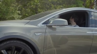 Genç adam konuşmak ile modern arabada oturan onun kızı. Arka plan, orman arkasında sürme ve gülen insanlar. Ağır çekim.