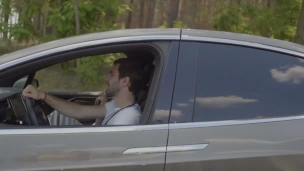 年轻人和他的女孩坐在现代汽车里聊天 人们正骑在森林后面的背景下 慢动作 — 图库视频影像