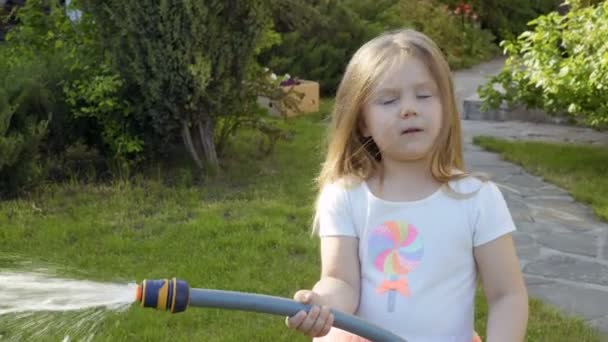 Little girl water a flower bed from a hose — Stock Video