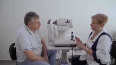 Doktor hasta ile görme kontrol prosedürü sonra konuşuyor. Adam neye optik modern cihazların yakınında oturan doktor.