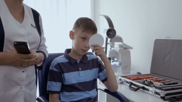 Oculist クリニックで少年の目を調べるします 子供彼の片目を閉じて 彼が見るものについて医者に教えてください — ストック動画