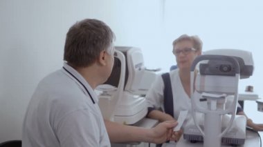 Doktor hasta ile görme kontrol prosedürü sonra konuşuyor. Adam neye optik modern cihazların yakınında oturan doktor.