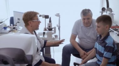Baba ve oğul dinleme ofiste oturan doktor. Opthalmological ekipman üzerinde arka plan vardır. Aile göz kliniği Resepsiyon.