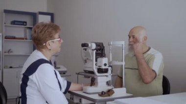 Doktor hasta ile görme kontrol prosedürü sonra konuşuyor. Adam neye optik modern cihazların yakınında oturan doktor.