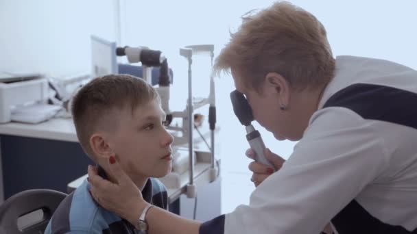 医師は 患者の目をランプでチェックします 眼科の受付で小さな男の子 — ストック動画