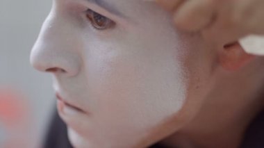 Genç adam, yüzünde beyaz boya koymak. Sokak MIME kentsel sokaklarda Show'da hazırlanın. Yakışıklı genç amatör insanlar küçük sahneler gösteriyor para kazanmak.