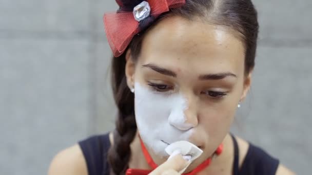 小女孩在脸上涂上白色的颜料 街头哑剧演员准备在城市街道上表演 美丽的年轻业余挣钱显示人小场面 — 图库视频影像