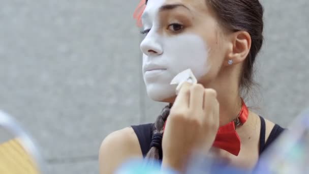 小女孩在脸上涂上白色的颜料 街头哑剧演员准备在城市街道上表演 美丽的年轻业余挣钱显示人小场面 — 图库视频影像