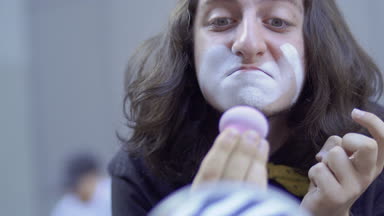 Genç adam, yüzünde beyaz boya koymak. Sokak MIME kentsel sokaklarda Show'da hazırlanın. Yakışıklı genç amatör insanlar küçük sahneler gösteriyor para kazanmak.