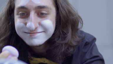 Genç adam, yüzünde beyaz boya koymak. Sokak MIME kentsel sokaklarda Show'da hazırlanın. Yakışıklı genç amatör insanlar küçük sahneler gösteriyor para kazanmak.