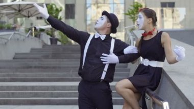 İki komik pandomim bir sahne Ofis Merkezi yakınındaki merdiven oynamak. Kız ve adam gesticulates eller ve yüz ifadeleri. Genç Amatör insanlar küçük komik sahneler, kentsel gösteriyor para kazanmak