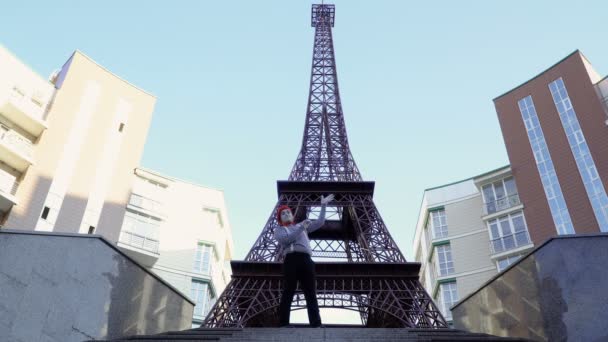Muž na sobě mime svlékl košili a červený baret pózuje pro kameru v blízkosti Eiffelovy věže. Pouliční herec vydělat peníze zábavné role hrát a hrát si s jeho výrazy obličeje.