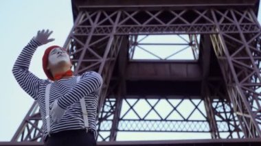 O adam MIME giymiş gömlek çıkardı ve kırmızı bere Eiffel tower yakınındaki kamera için poz. Sokak aktör komik roller oynayan ve onun yüz ifadeleri ile oynarken para kazanmak.