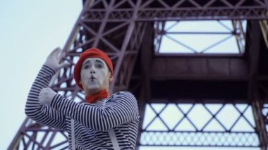 O adam MIME giymiş gömlek çıkardı ve kırmızı bere Eiffel tower yakınındaki kamera için poz. Sokak aktör komik roller oynayan ve onun yüz ifadeleri ile oynarken para kazanmak.