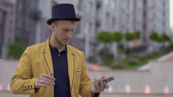 Иллюзионист в шляпе и желтой куртке умело двигает игральными картами в руках — стоковое видео