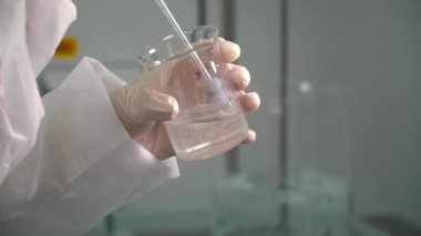 Kimyager viskoz sıvı bir balonun içinde bir cam tüp ile karıştırma. Laboratuvar çalışan sıvı deneme için hazırlanıyor. Yakın çekim yakışıklı.