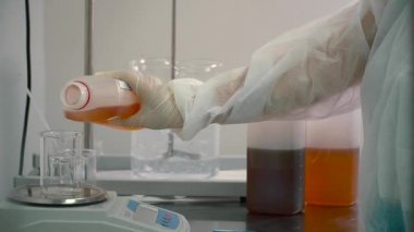 Elektronik ölçekte bir şişesi içine portakal sıvı dökme kimyager. Bilim adamı Deney Laboratuvar donatımı hazırlanıyor. İlaç otomatik blender, sıvıları karıştırma