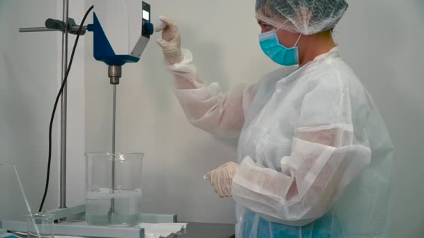 化学実験室の混合装置を調整します 液中翼機と混合液を見てボタンを移動する女性 ガラスのコップの液体を混ぜてミキサー — ストック動画