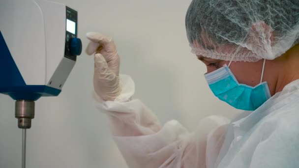 化学家在实验室调整混合设备 女人在机器上移动按钮 看着桌子上杯子里的搅拌机 — 图库视频影像