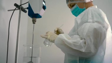 Kimyager viskoz sıvı bir balonun içinde bir cam tüp ile karıştırma. Laboratuvar işçi Ekle altında çalışma ilaç makine karıştırma bir sıvı içine jel.