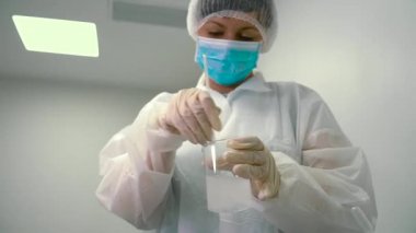 Kimyager viskoz sıvı bir balonun içinde bir cam tüp ile karıştırma. Laboratuvar çalışan sıvı deneme için hazırlanıyor. Kadın vermek onun meslektaşım loşluğa.