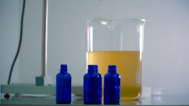 Turuncu sıvı ile cam ölçü fincan ve üç şişe yakın. Kamera çekimde. Yakın çekim. Laboratuvar donatımı.