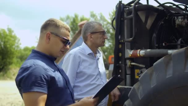 Rolnik przeprowadza inspekcję ciągnika z zewnątrz i rozmowy ze sprzedającym — Wideo stockowe