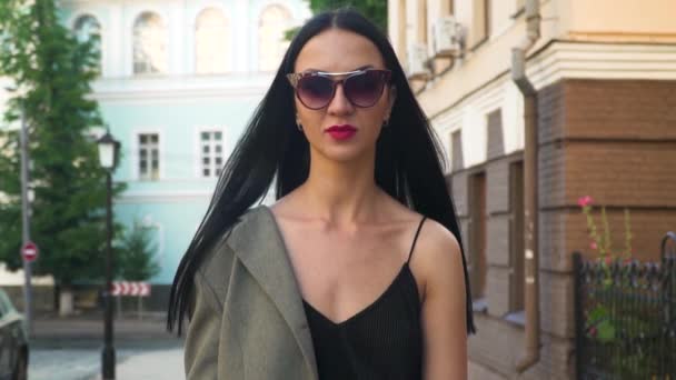 Молода стильна жінка в сонцезахисних окулярах ходить на камеру в повільному русі — стокове відео