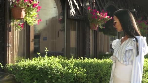 Элегантная женщина в солнечных очках ходит по улице с маленькими магазинами в городе — стоковое видео