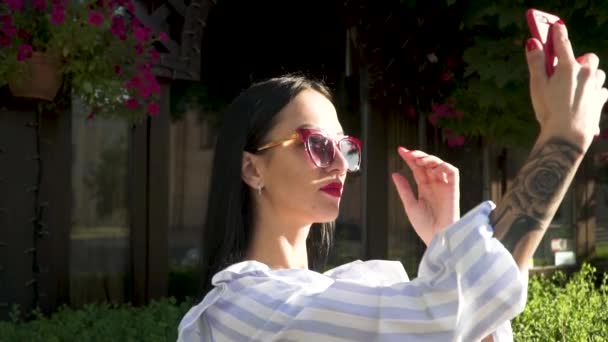 Κομψό μελαχρινή με tattoed χέρι σε γυαλιά ηλίου κάνει selfie στο τηλέφωνο στην πόλη — Αρχείο Βίντεο