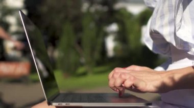 Beyaz soyulmuş bluz şık kadın Parkı ve onu laptop yazarak bir bankta oturuyor. Şık iş kadını onun bilgisayarda açık havada doğa üzerinde çalışıyor.