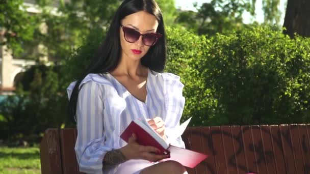 Elegante donna in occhiali da sole leggere libro nel parco — Video Stock