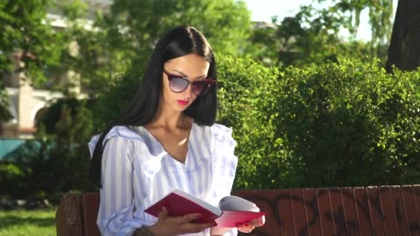 Hermosa morena acabada de leer libro en el parque — Vídeos de Stock