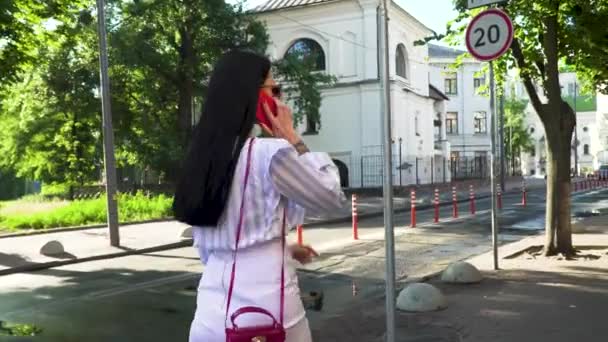 Femme élégante en vêtements blancs parlant au téléphone et marchant dans la rue urbaine — Video