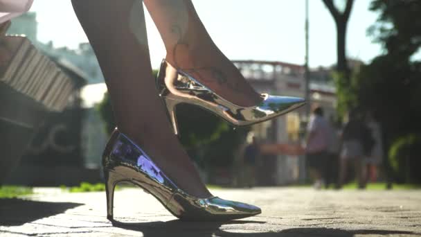 Жіночі ноги в срібному взутті на високих підборах, сидячи на лавці — стокове відео