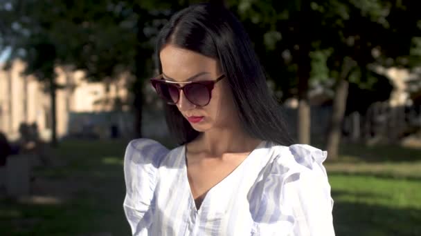 Красива молода жінка в сонцезахисних окулярах друкує на ноутбуці в парку — стокове відео