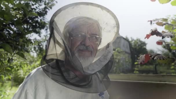 Beekeeper in protective veil and hat is looking at camera and smiling — Stock Video