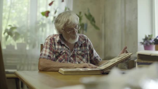 Зрелый человек смотрит свой альбом со старыми фотографиями дома — стоковое видео