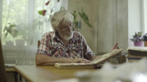 Volwassen man die van zijn album met oude foto's thuis — Stockvideo