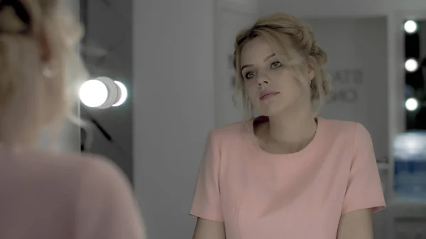 สาวสวยอ่อนโยนในชุดสีชมพู มองไปที่กระจกในห้องแต่งหน้า — ภาพถ่ายสต็อก