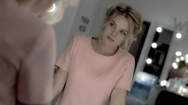 Kaunis tyttö vaaleanpunainen mekko meikki poseeraa kameran edessä peili — kuvapankkivalokuva