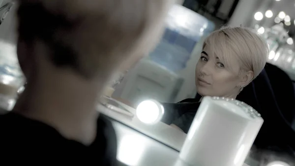 Kaunis nainen, jolla on lyhyt kampaus ja kasvojen lävistys katso peiliin itseensä — kuvapankkivalokuva