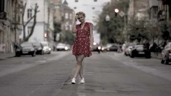 Sjarmerende blond i lys kjole som poserer for kamera på veien stockbilde