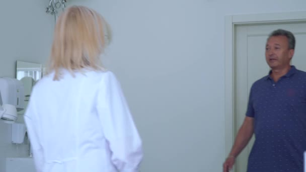 Доктор приветствует взрослого мужчину в ее кабинете — стоковое видео