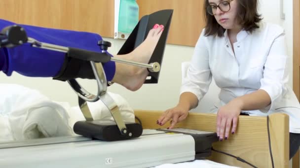 Médico controla a perna do paciente durante o procedimento de mecanoterapia — Vídeo de Stock