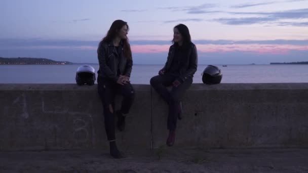 Twee jonge meisjes fietsers zitten op zee achtergrond en ontspannen aan de dijk — Stockvideo