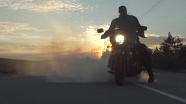 Motorcu bir motosiklet yolda, arka plan gün batımı ile çok duman oluşturmak